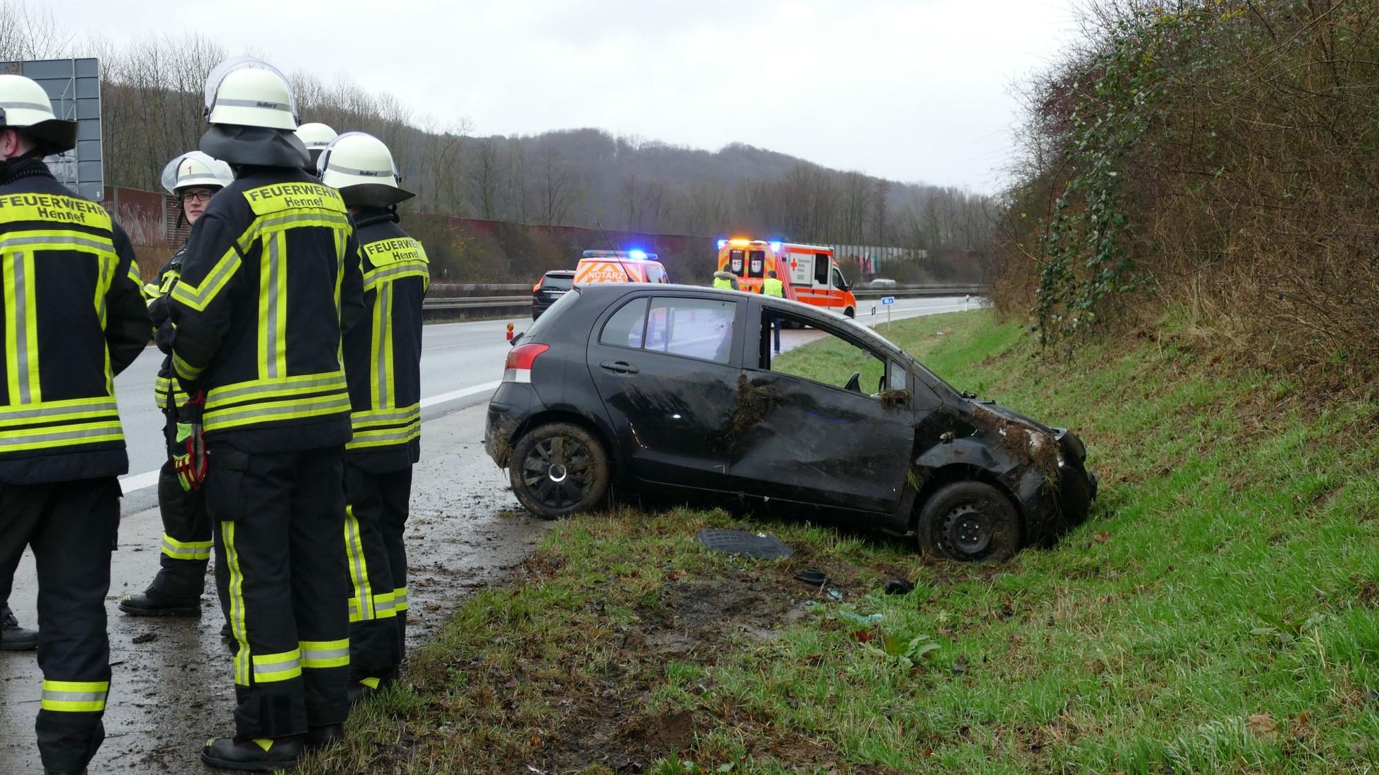 Feuerwehrleute stehen auf der Autobahn neben einem beschädigten Kleinwagen.