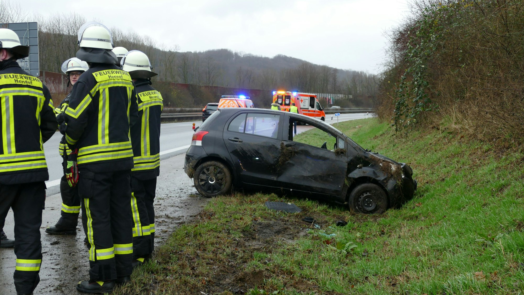 Feuerwehrleute stehen auf der Autobahn neben einem beschädigten Kleinwagen.