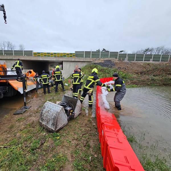 Feuerwehrleute legen Sandsäcke auf eine mobile Wand aus Plastik.