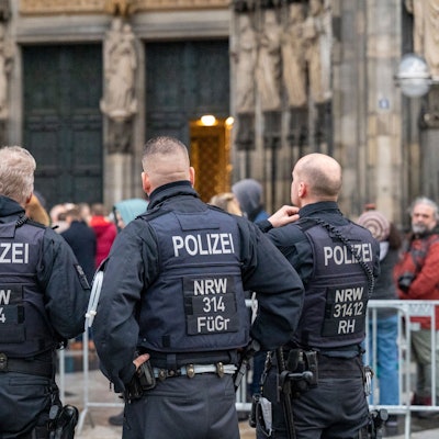 Köln: Wegen eines befürchteten Anschlags kontrolliert die Polizei alle Besucher des Doms. Zu sehen sind die Hinteransichten von vier Polizisten vor dem Hauptportal des Doms.