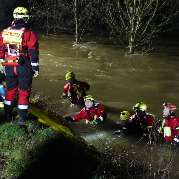 Angehörige des DLRG in Tauchanzügen und Helmen mit Kopflampen stehen bis zur Brust im reißenden Fluss.
