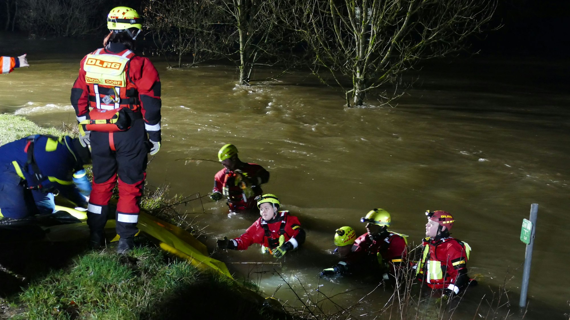 Angehörige des DLRG in Tauchanzügen und Helmen mit Kopflampen stehen bis zur Brust im reißenden Fluss.