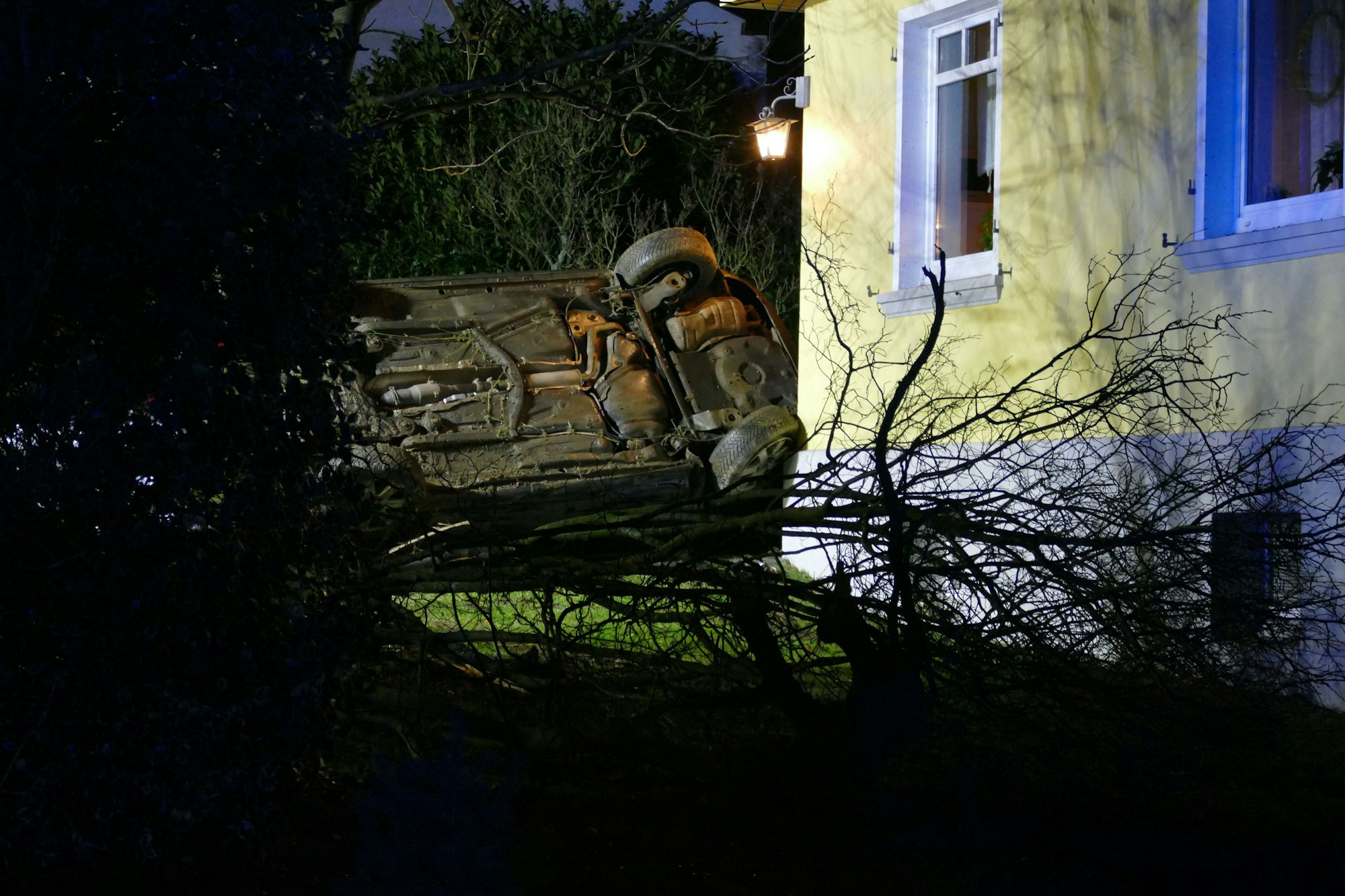 Ein Auto liegt neben einer Hauswand auf der Seite.