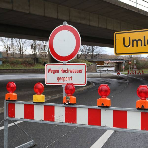 Eine rot-weiße Warnbake mit dem Hinweis auf das Hochwasser steht auf einer Straße.