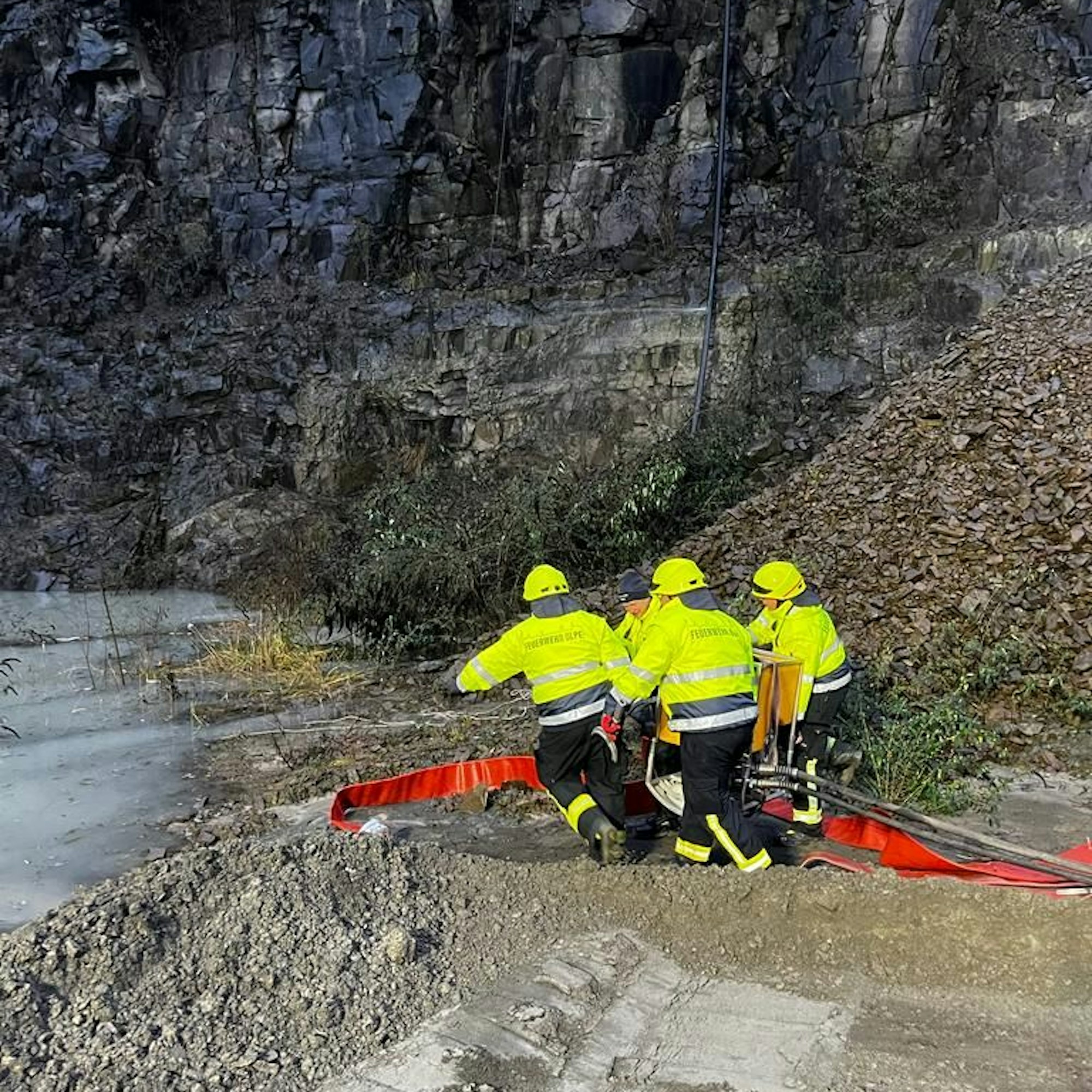 Feuerwehrleute tragen eine leistungsstarke Pumpe zu einem überfluteten Steinbruch.