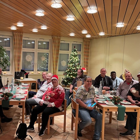 Menschen sitzen an gedeckten Tischen, im Hintergrund steht ein Weihnachtsbaum.