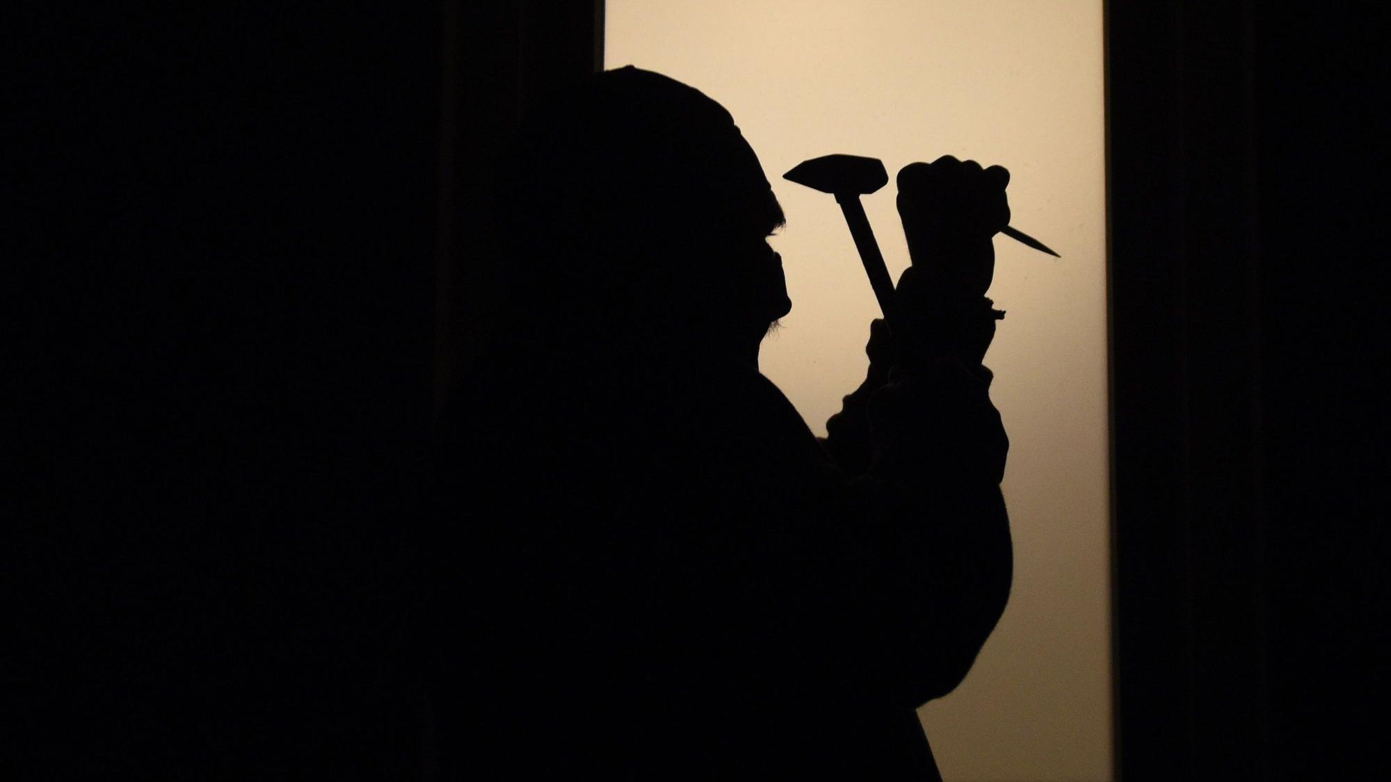 Schatten eines Mannes, der mit einem Hammer auf eine Scheibe schlägt