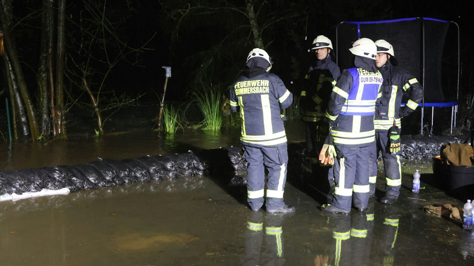 Mehrere Feuerwehrleute stehen im Wasser. Im Hintergrund sind aufgestapelte Sandsäcke zu sehen.