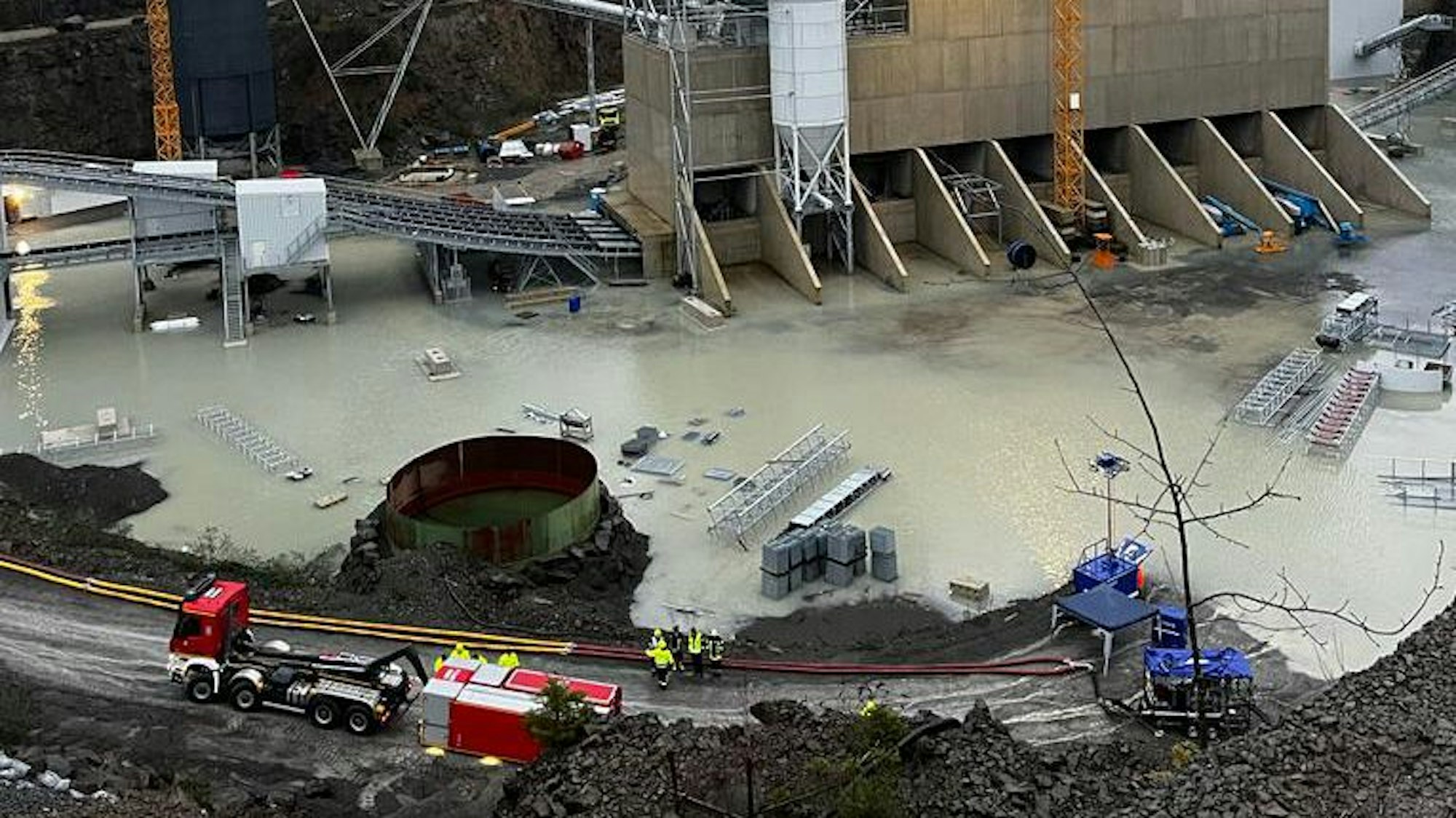 Ein Feuerwehrfahrzeug mit einem Abrollcontainer und Schläuchen steht neben einem gefluteten Steinbruch.