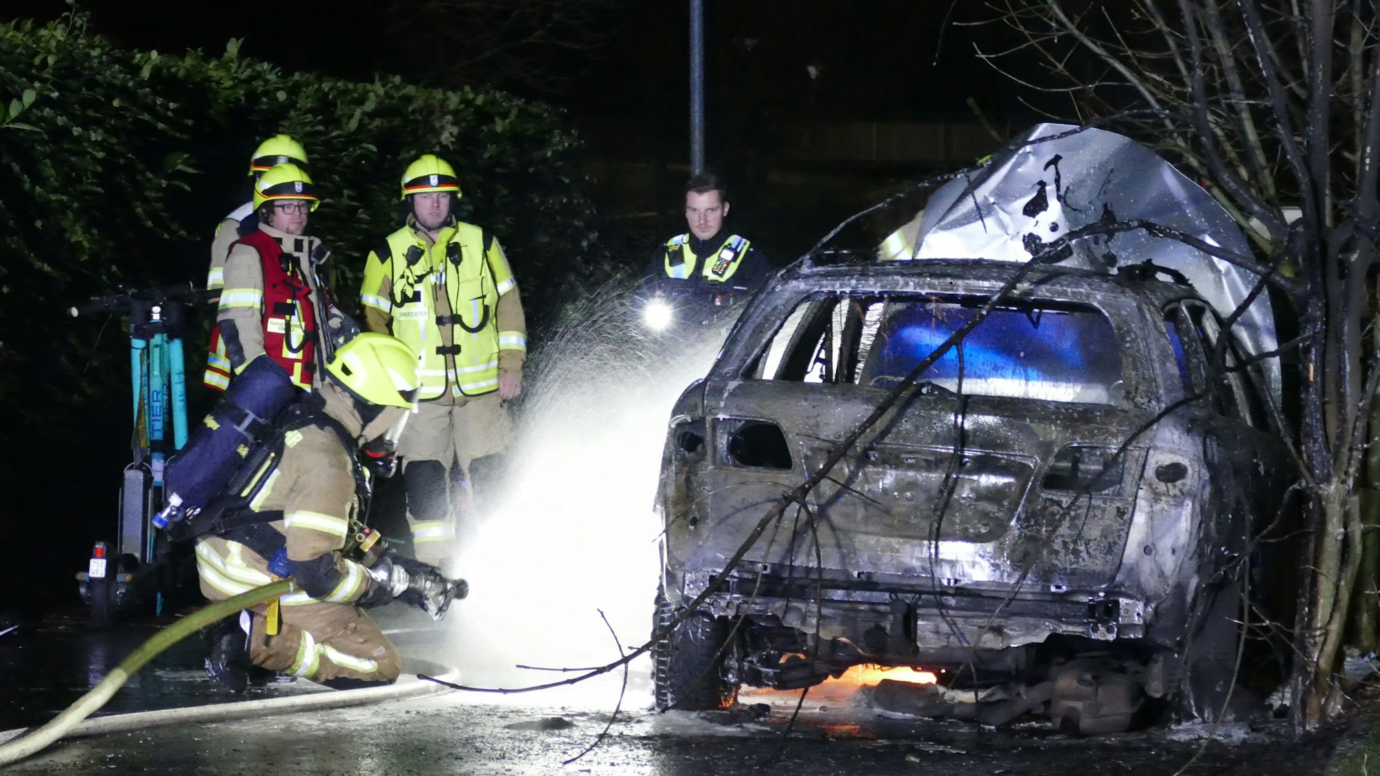 Feuerwehrleute löschen einen bereits weitgehend ausgebrannten Pkw.