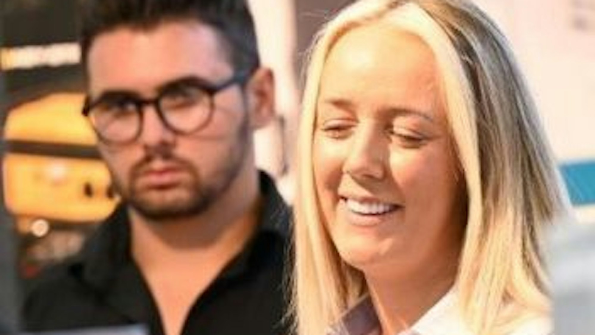 Neben einem Mann mit Brille steht eine blonde Frau.