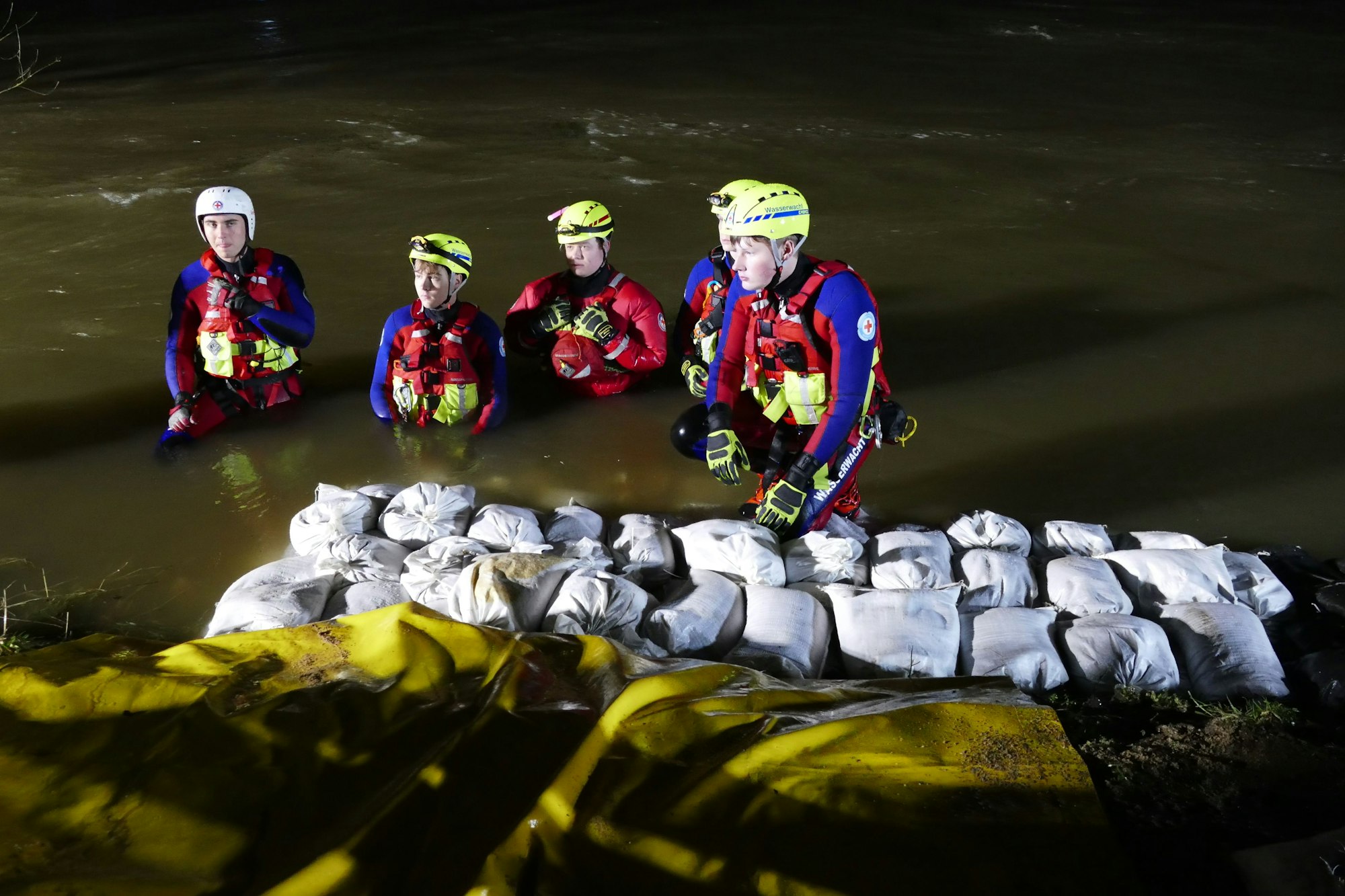 Vier Strömungsretter stehen im Wasser, vor ihnen sind Sandsäcke aufgeschichtet.