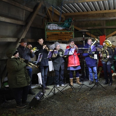 Ein Posaunenchor spielt in einer Remise eines landwirtschaftlichen Betriebs.