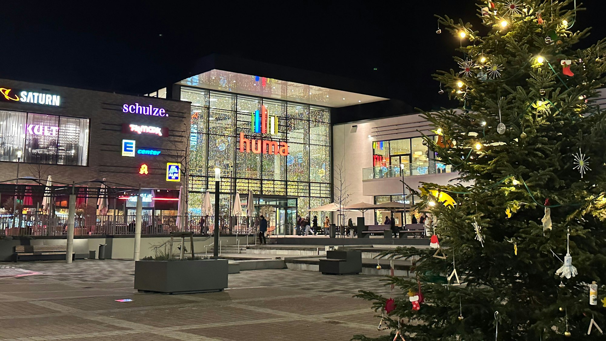 Blick auf das Huma-Einkaufszentrum mit einem beleuchteten Tannenbaum im Vordergrund.