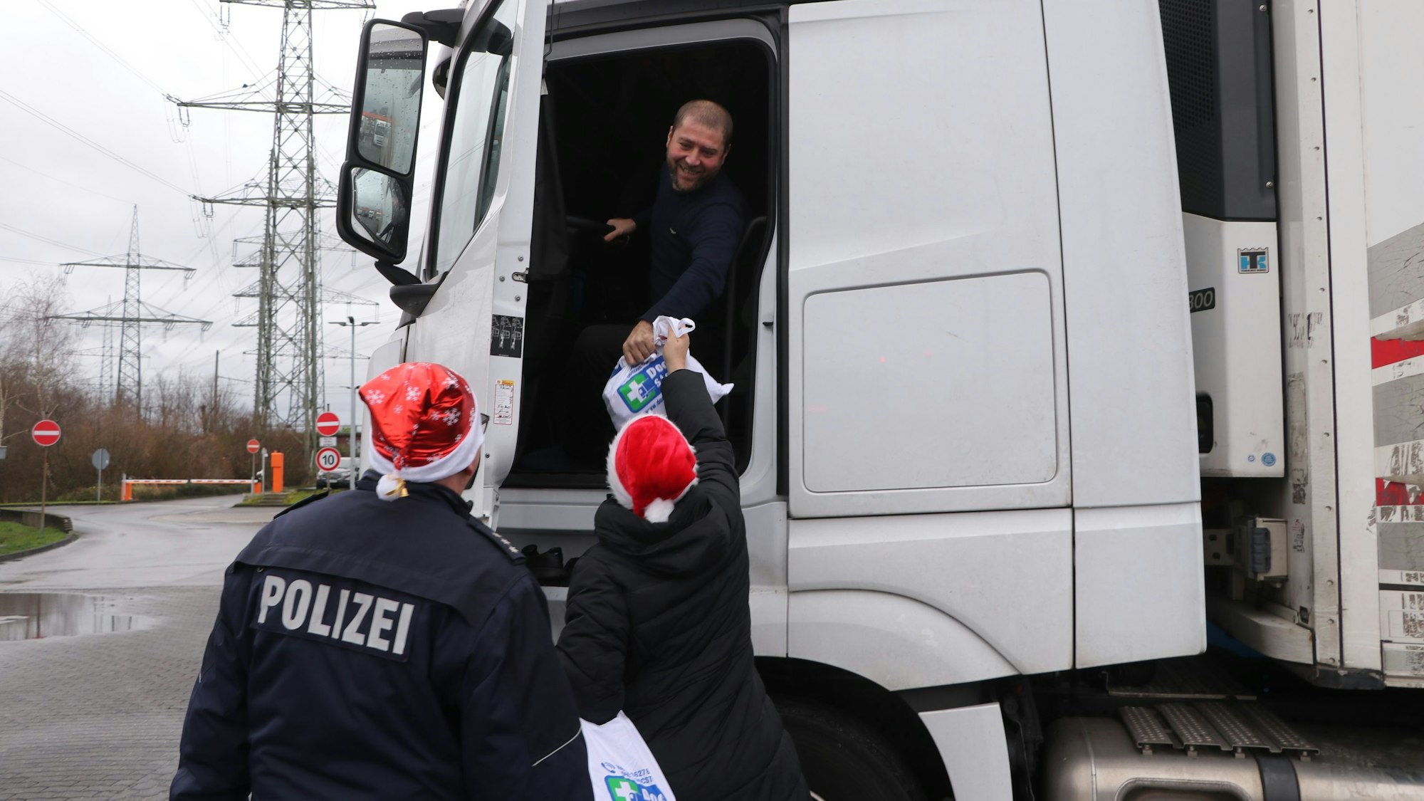 Polizisten reichen einem Fernfahrer eine Tüte in seinen Lkw.