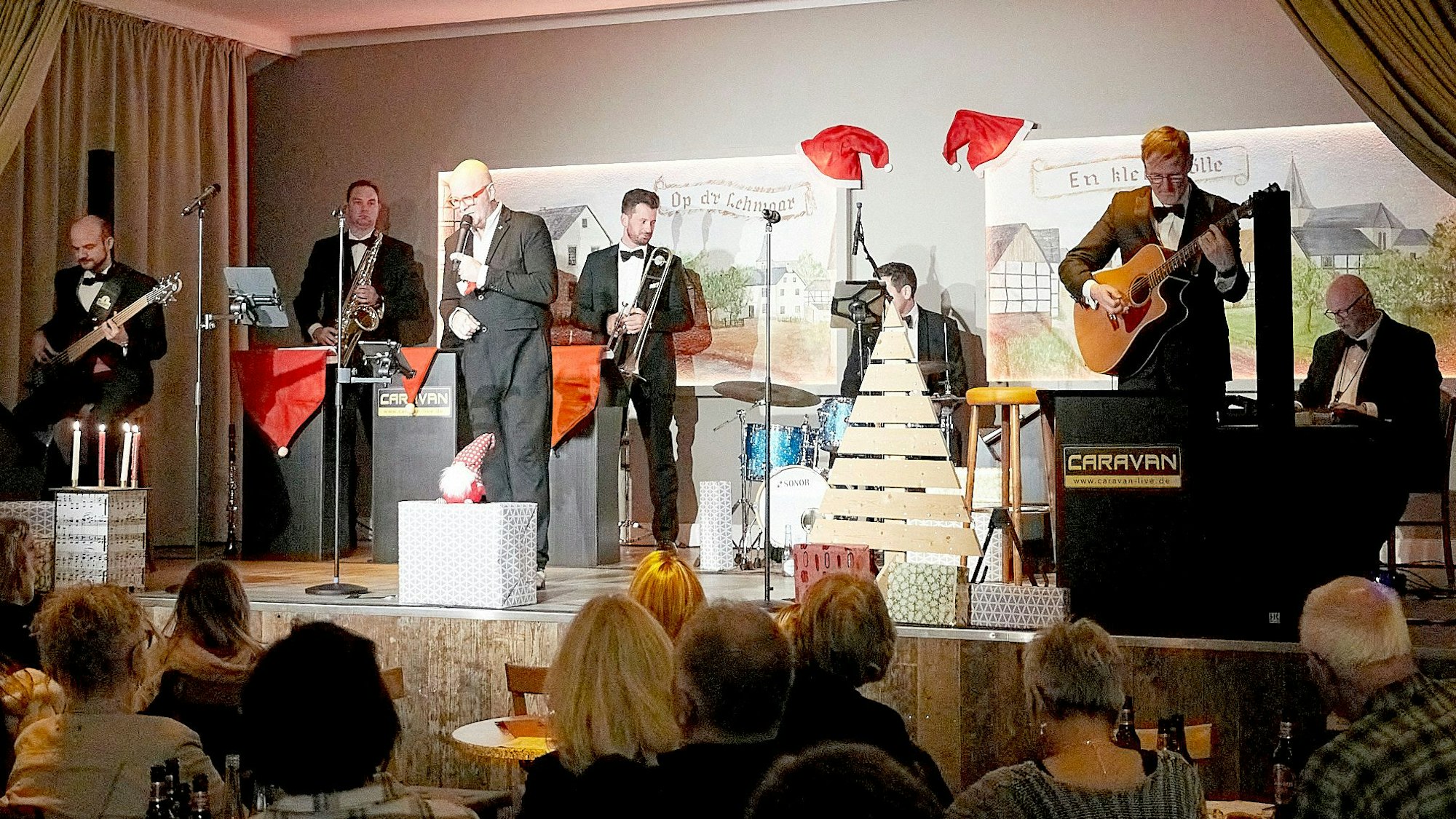 Die Band, gekleidet in Smokings, steht auf der Bühne und musiziert.