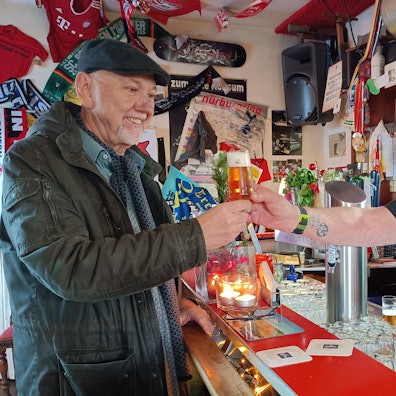 Wirt Andreas Weyrauch reicht einem Gast ein Kölsch im Pilsglas.