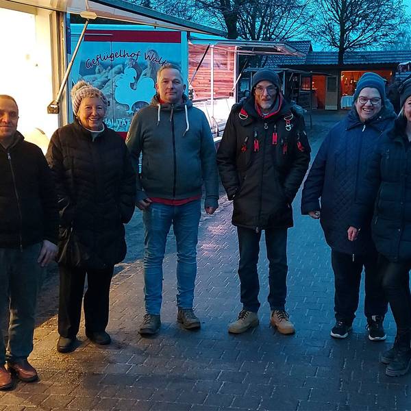 Einige Männer und Frauen stehen in der Abenddämmerung an einem Verkaufsstand auf dem letzten Markt in Ripsdorf.