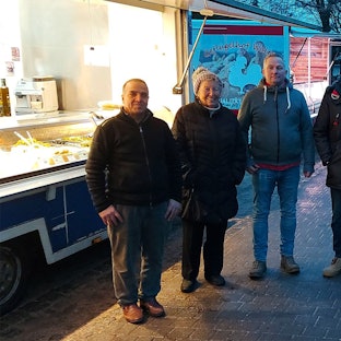 Einige Männer und Frauen stehen in der Abenddämmerung an einem Verkaufsstand auf dem letzten Markt in Ripsdorf.