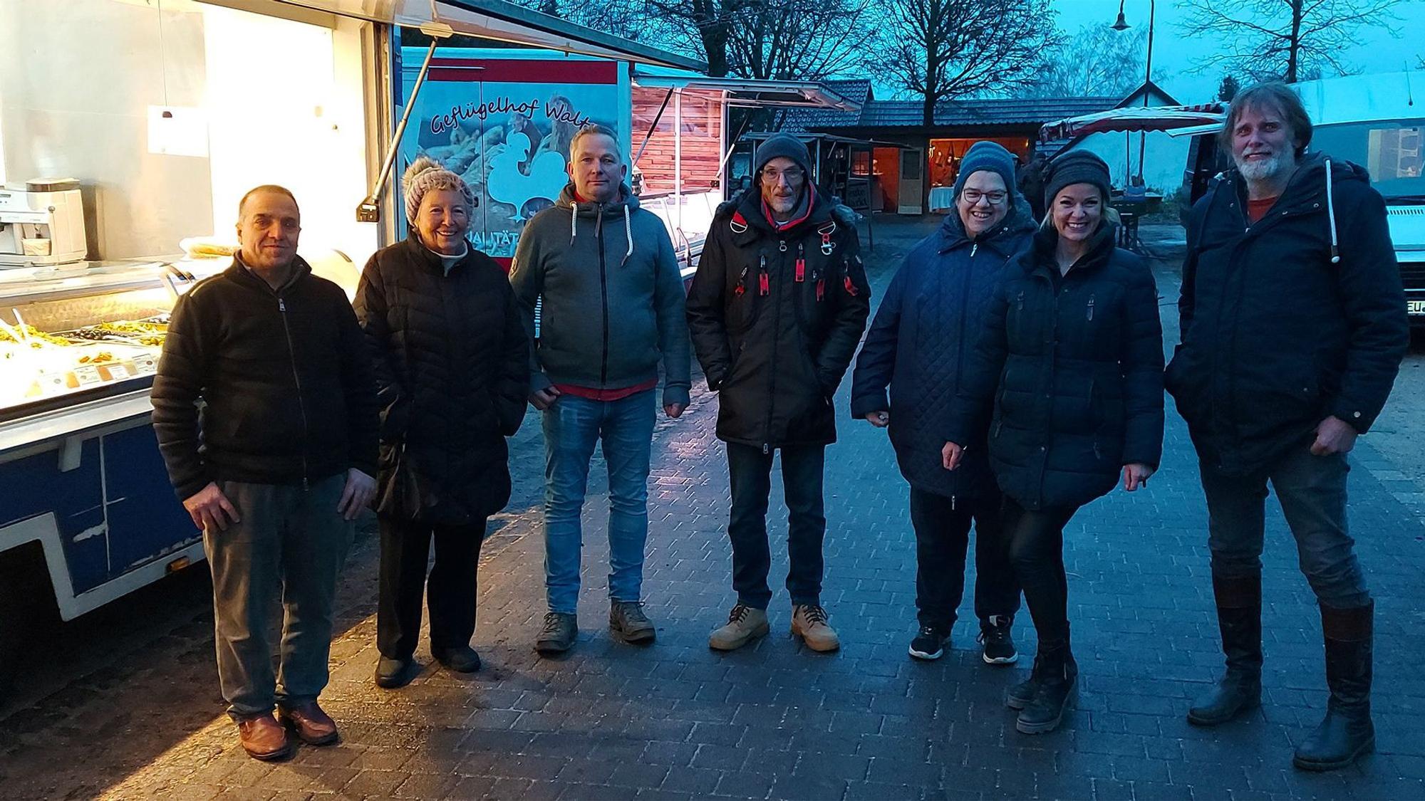 Einige Männer und Frauen stehen in der Abenddämmerung an einem Verkaufsstand auf dem letzten Markt in Ripsdorf.