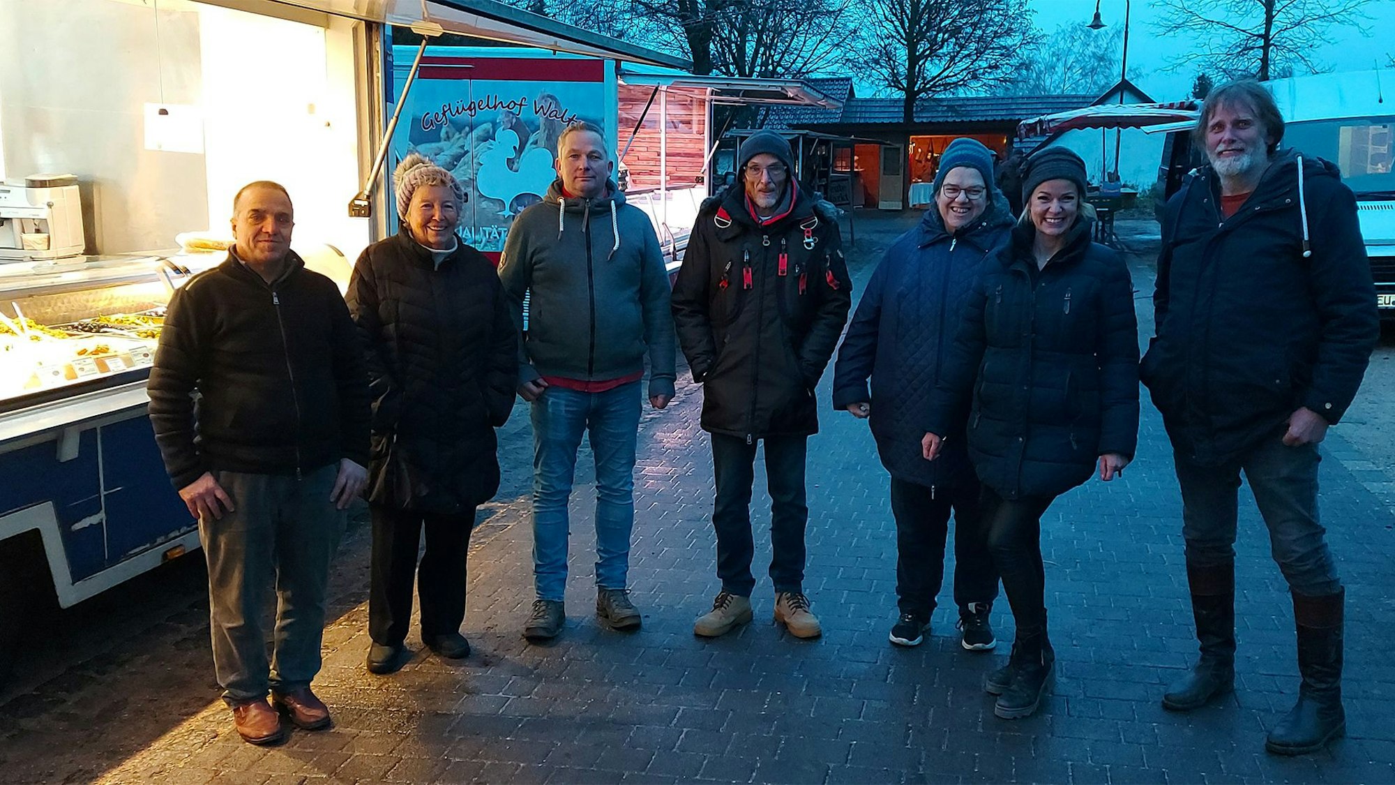 Einige Männer und Frauen stehen in der Abenddämmerung an einem Verkaufsstand auf dem letzten Markt in Ripsdorf.