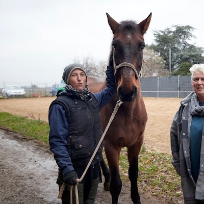 Nina Aschhoff und Bettina Kossmann stehen an einem Außenreitplatz. Nina Aschhoff hält ein Pferd am Halfter.