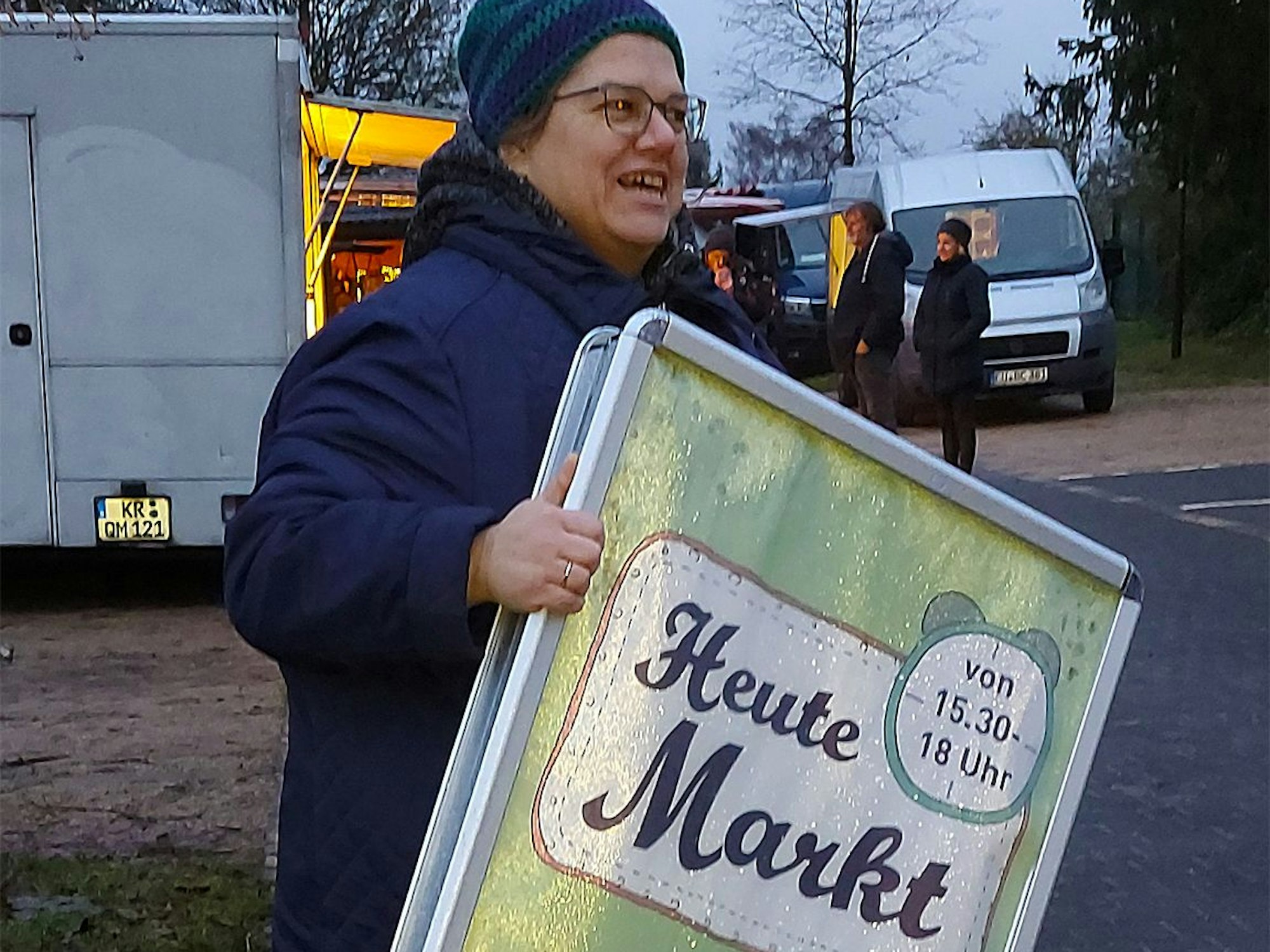 Andrea Ehlen hat das Klappschild in der Hand, das auf den Markt in Ripsdorf hinweist.