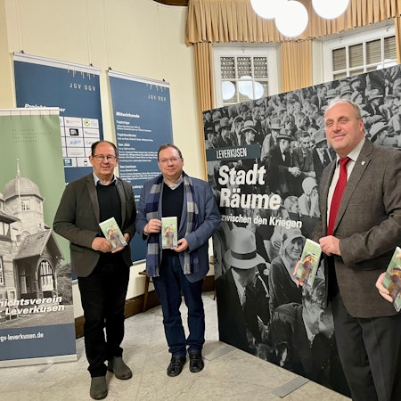 Uwe Bräutigam, Guido von Büren, Michael Gutbier und Ernst Küchler von den Geschichtsvereinen aus Opladen und Jülich vor dem Plakat für das Ausstellungsprojekt „Stadträume“ in der Villa Römer