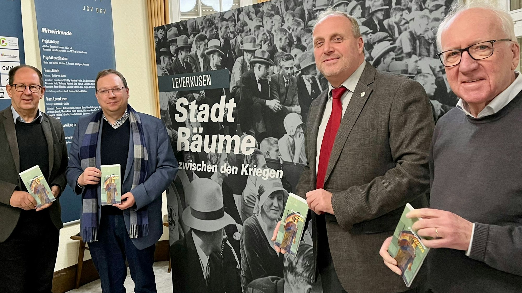 Uwe Bräutigam, Guido von Büren, Michael Gutbier und Ernst Küchler von den Geschichtsvereinen aus Opladen und Jülich vor dem Plakat für das Ausstellungsprojekt „Stadträume“ in der Villa Römer