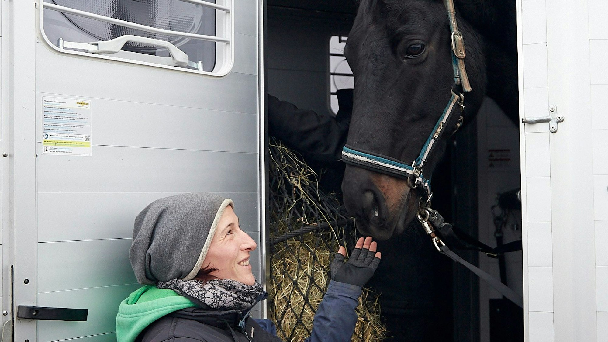 Nina Aschhoff steht an der Tür eines Transporters, in dem sich ein schwarzes Pferd befindet.