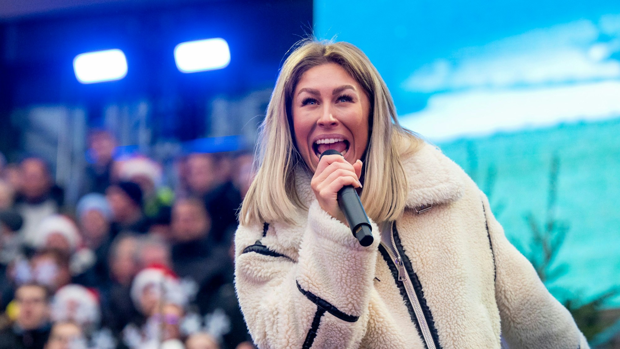 Die Sängerin Linda Teodosiu ist bei einer Probe für Looss mer Weihnachtsleeder singe im Stadion zu sehen. Sie trägt eine weiße Teddyjacke.