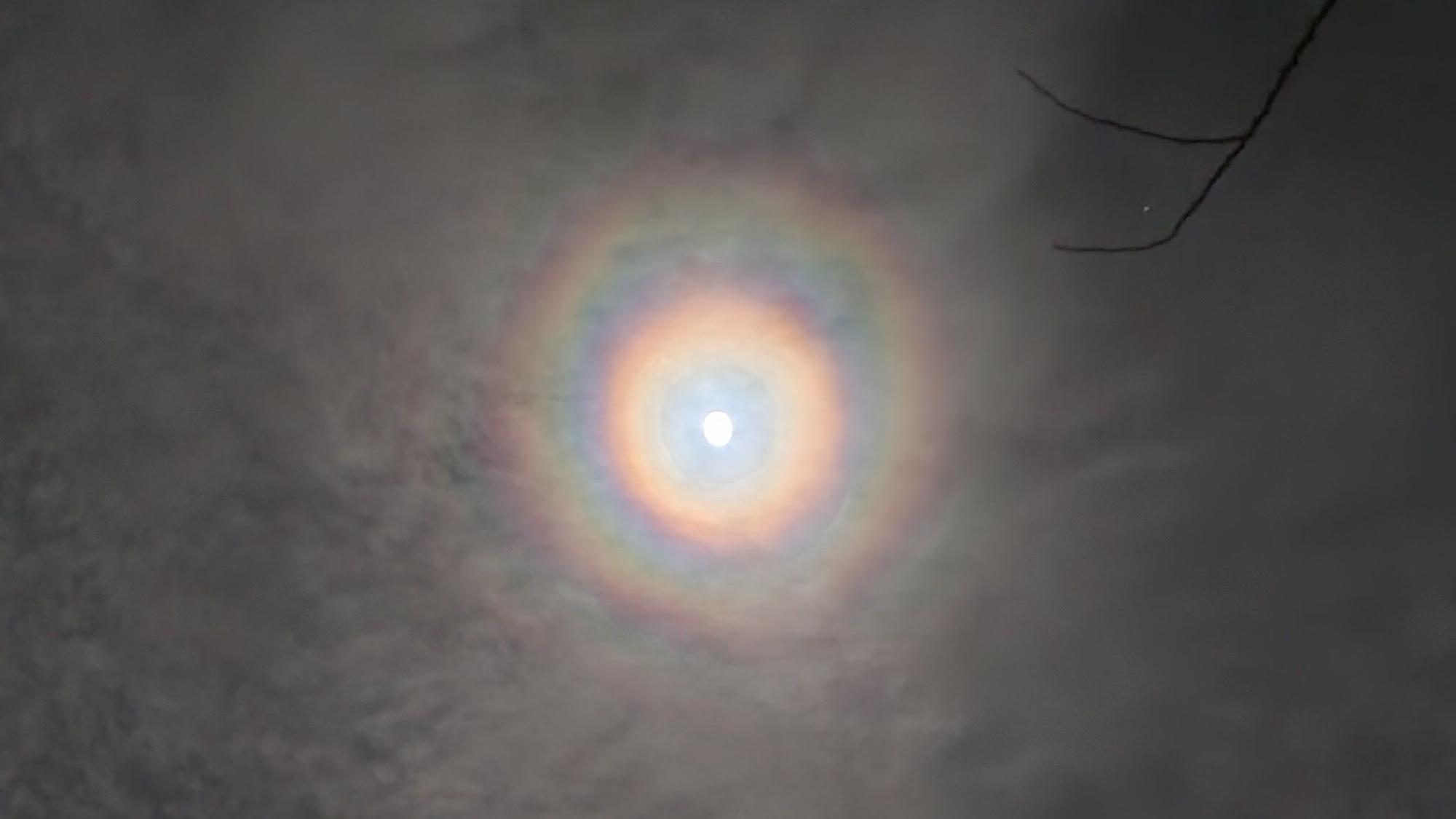 Zu sehen ist ein Vollmond mit Ringen, von leichten Wolken verdeckt.