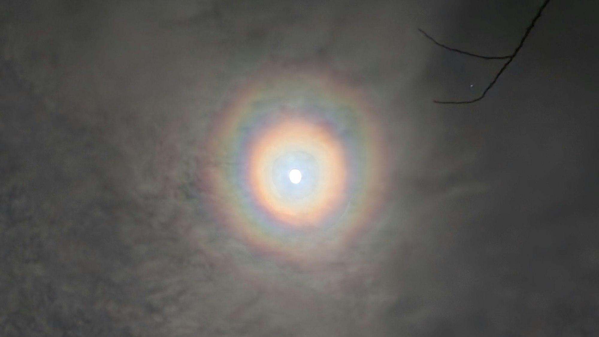 Zu sehen ist ein Vollmond mit Ringen, von leichten Wolken verdeckt.