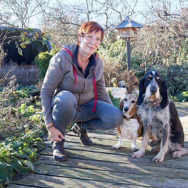 Franziska Weyer hockt in einem Garten neben zwei Hunden, einem Basset und einem Griffon.