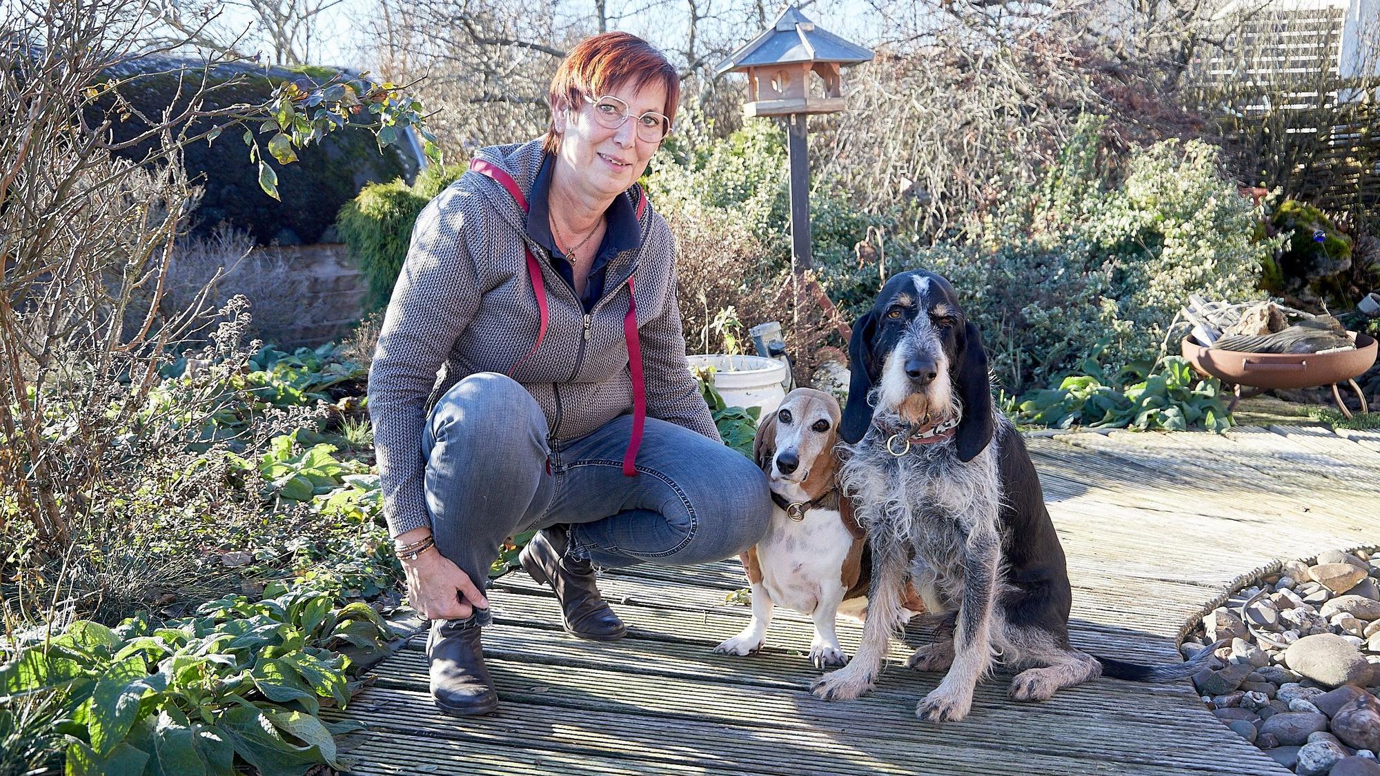 Franziska Weyer hockt in einem Garten neben zwei Hunden, einem Basset und einem Griffon.