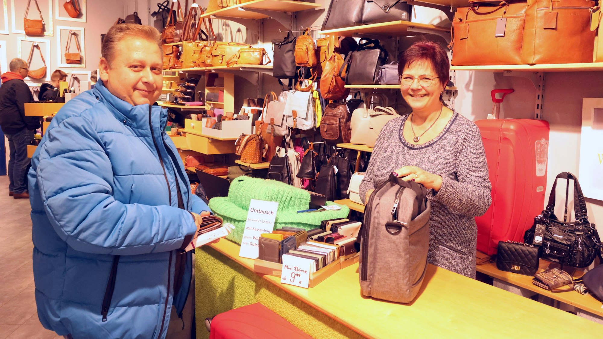 Ein Mann kauft in einem Geschäft eine Tasche. Er wird von einer Verkäuferin bedient.