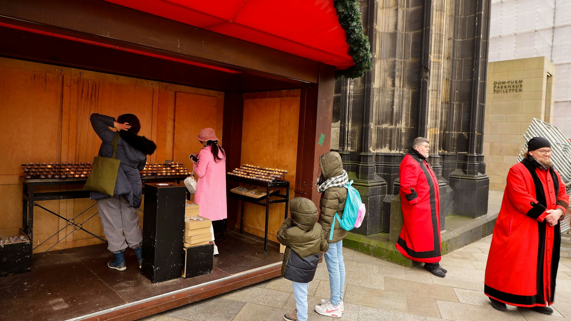 Menschen stehen vor einer Weihnachtsmarkthütte. Drinnen entzünden sie Kerzen.