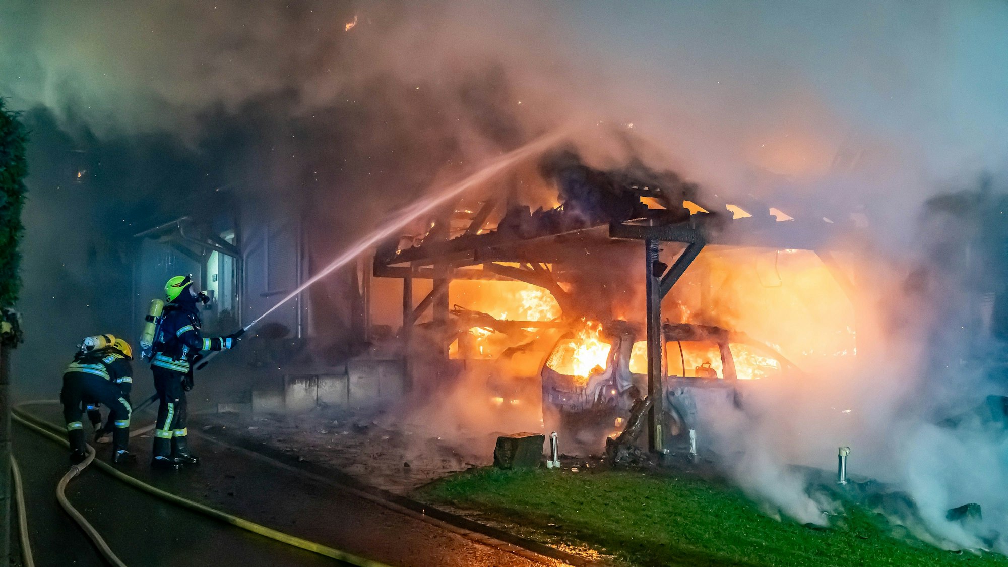Ein Feuerwehrmann löscht einen lichterloh brennenden Carport.