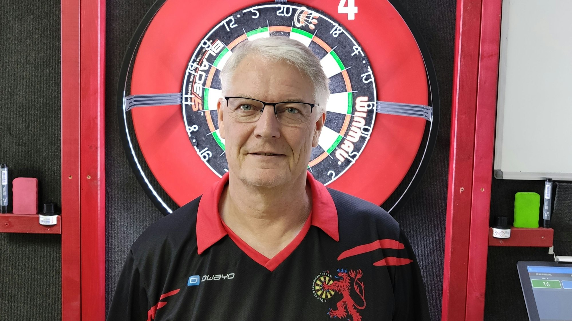 Thomas Walsh
steht vor einer Dartscheibe und lächelt in die Kamera.