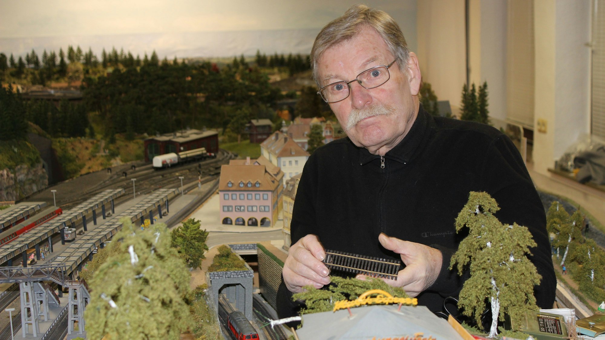 Ein Mann sitzt inmitten einer Modelleisenbahn-Landschaft.
