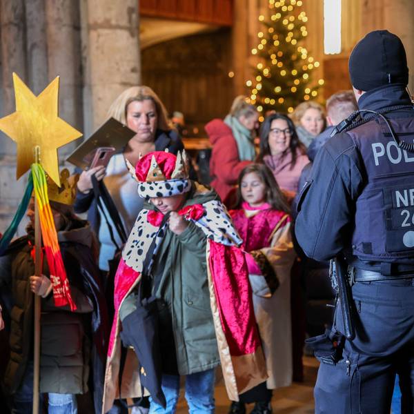 Zu sehen in ein Polizeibeamter vor verkleideten jungen Kindern. Es geht um die Aussendung der Sternsinger im Kölner Dom.