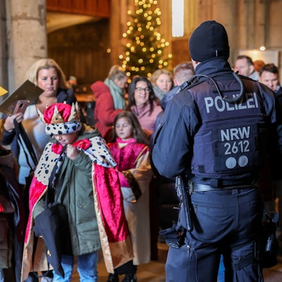 Zu sehen in ein Polizeibeamter vor verkleideten jungen Kindern. Es geht um die Aussendung der Sternsinger im Kölner Dom.