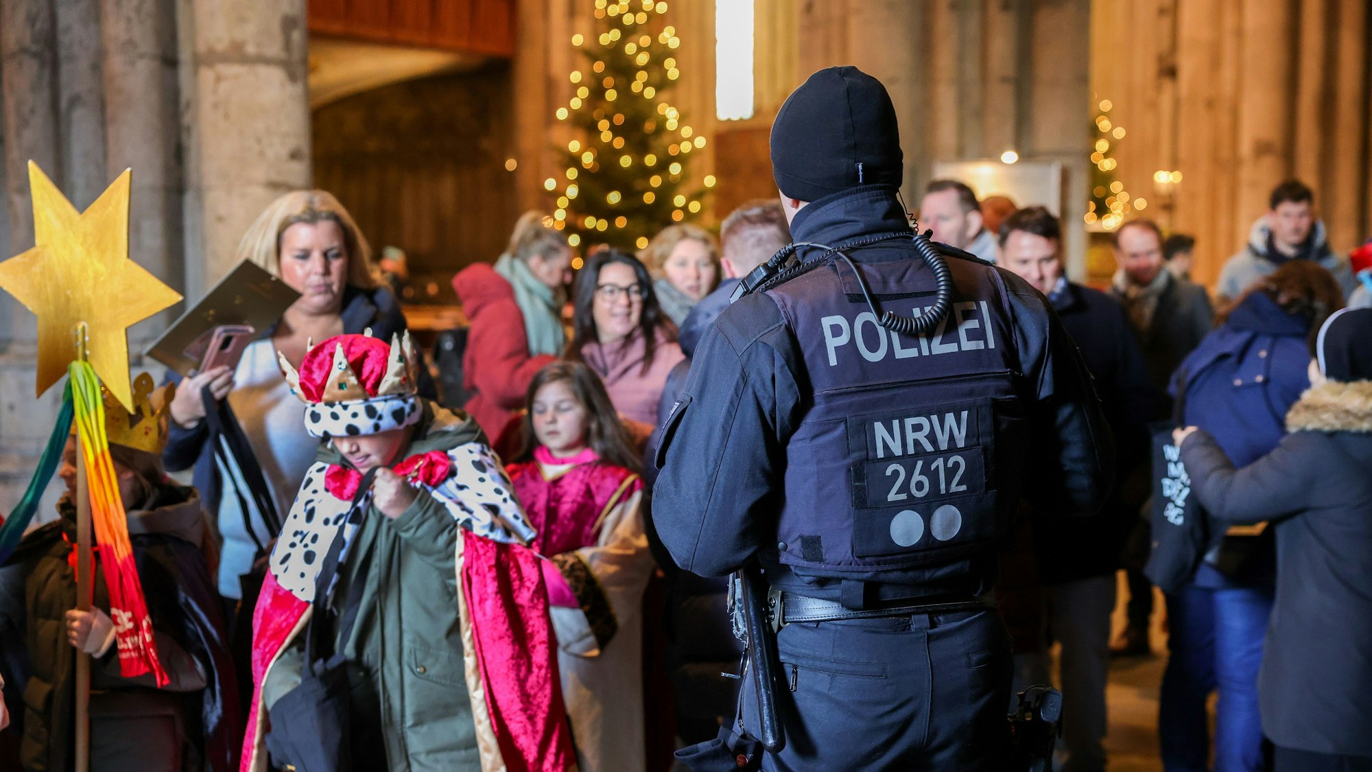 Zu sehen in ein Polizeibeamter vor verkleideten jungen Kindern. Es geht um die Aussendung der Sternsinger im Kölner Dom.