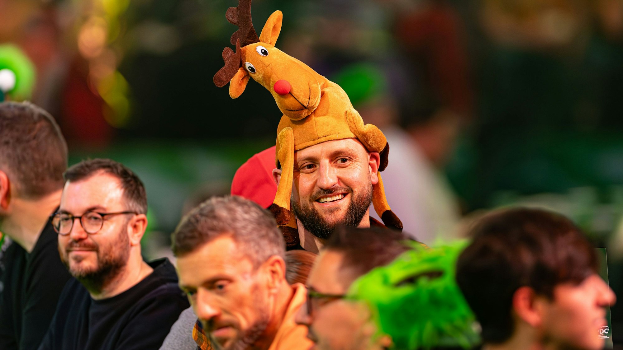 Bei der Darts-WM in London erwarten verkleidete Fans die Spieler. Ein Mann trägt eine Elch-Mütze.