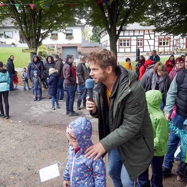 Der Kinderliedersänger Uwe Reetz hält ein Mikrofon in der Hand. Um ihn herum stehen einige Kinder mit ihren Eltern.