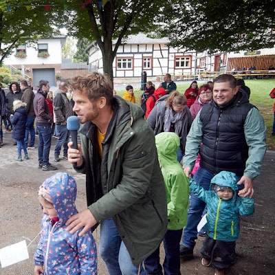 Der Kinderliedersänger Uwe Reetz hält ein Mikrofon in der Hand. Um ihn herum stehen einige Kinder mit ihren Eltern.