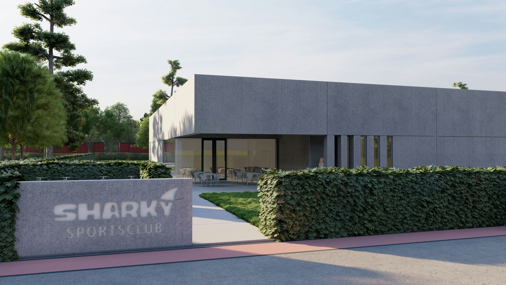 Das Bild zeigt einen modernen Bau, dessen Eingangsbereich mit viel Glas gestaltet ist. Vor dem Gebäude steht ein Stein mit der Aufschrift „Sharky Sportsclub“. An einer Hecke und einer Wiese vorbei führt der Weg zum Eingang.