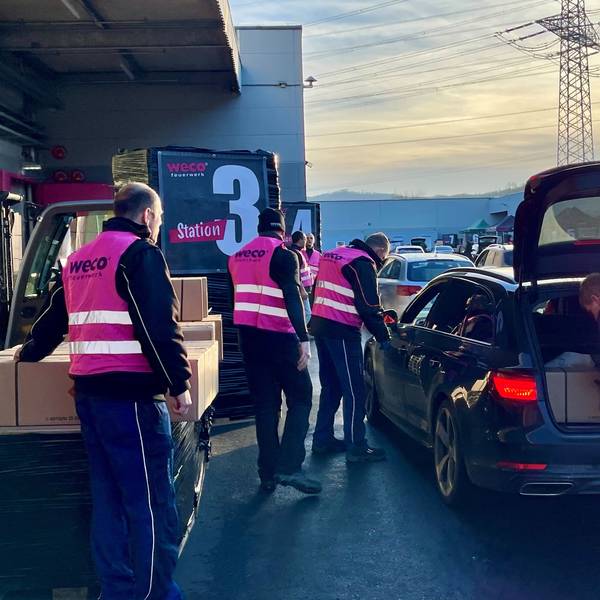 Männer in pinkfarbenen Weco-Westen beladen ein Auto mit langen Paketen.