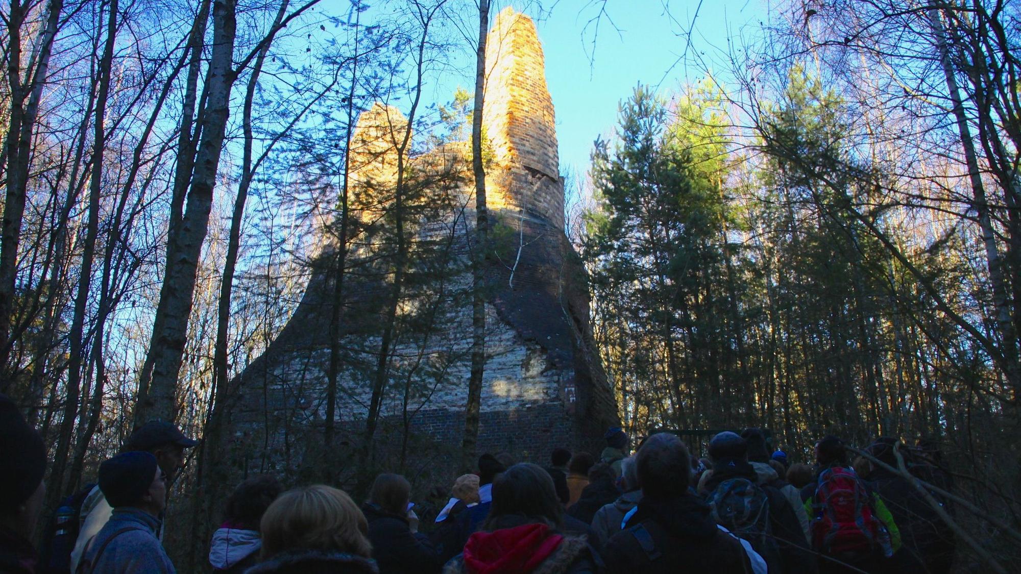 Eine Gruppe Menschen steht im Schatten, umgeben von Bäumen und von der Sonne beschienen ist der Lange Emil, ein Relikt aus der Bergbauzeit in Mechernich.