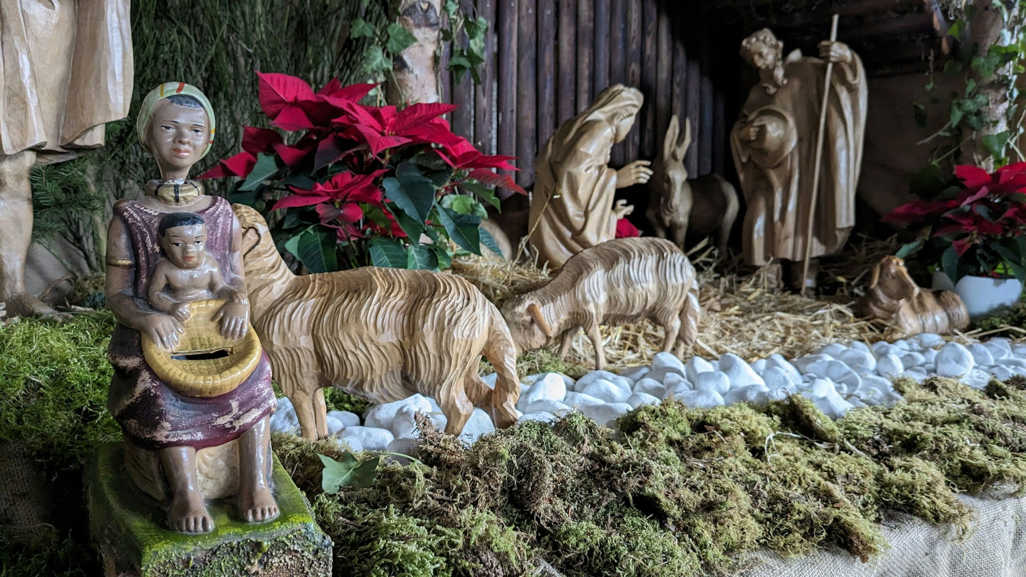 Eine Missionsspardose (li.), die eine dunkelhäutige Frau mit einem Kind auf dem Schoß darstellt, ist Teil der Kirchenkrippe der Pfarrkirche St. Martin in Nettersheim.